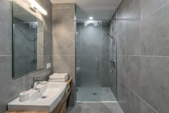 Salle de bains moderne avec luminaire IP44 au-dessus d'un miroir de vanité, carrelage gris et douche en verre dépoli